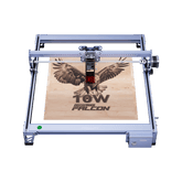 The Creality Falcon CR 10W Diode Laser Engraver, featuring advanced safety features, etches a flying falcon image and "10W Falcon" text onto a wooden board, viewed from above.