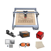The Creality Falcon Falcon CR 5W Diode Laser Engraver etches wood with ultra-fine precision, shown with a rotary roller, safety goggles, orange enclosure, sample wood and metal sheets, and a laser module.