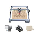 The Creality Falcon Falcon CR 5W Diode Laser Engraver showcases ultra-fine engraving precision on a wooden sheet with intricate designs, displayed with extra metal sheets, wooden sheets, markers, and a cylindrical rotating attachment.
