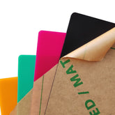 Four 12x12x1/8" frosted acrylic sheets by Creality Falcon Laser—orange, green, pink, and black—are stacked with top right corners visible; the black sheet shows a partially peeled brown protective film.