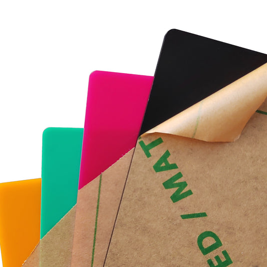 Four 12x12x1/8" frosted acrylic sheets by Creality Falcon Laser—orange, green, pink, and black—are stacked with top right corners visible; the black sheet shows a partially peeled brown protective film.