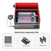 The image shows a red-framed Creality Falcon2 Pro 22W Enclosed Laser Engraver and Cutter with a pink floral design platform, boasting FDA Class 1 Safety Certification. Below are expansion kits: honeycomb workbench, rotary roller, and four raisers for enhanced engraving versatility.