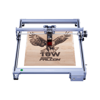 The Creality Falcon CR 10W Diode Laser Engraver, featuring advanced safety features, etches a flying falcon image and "10W Falcon" text onto a wooden board, viewed from above.