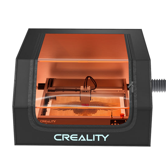 The image showcases a Creality Falcon laser engraver housed within a Falcon Protective Cover for Laser Engraver, featuring an orange viewing window. The machine is actively engraving an intricate design, with light visibly emitted from the laser, while a smoke expel system maintains a clear view and ensures safe operation. 1000