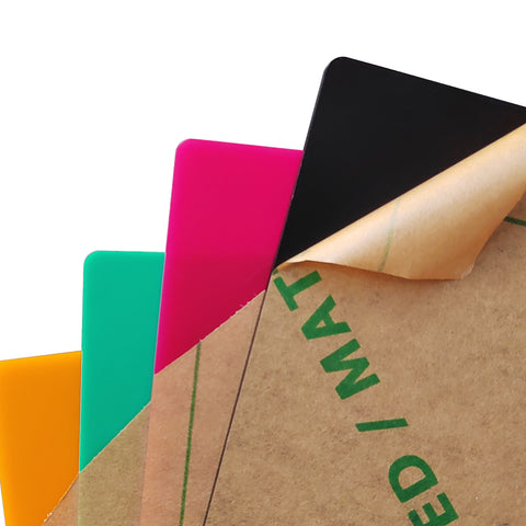 Four vibrant 12*12*1/8'' sheets from the Creality Falcon's Frosted Colorful Acrylic Sheets for Laser Engraver and Cutter set can be partially seen, with a protective brown overlay being removed to reveal the black, pink, green, and orange colors beneath—perfect for any laser cutting project.