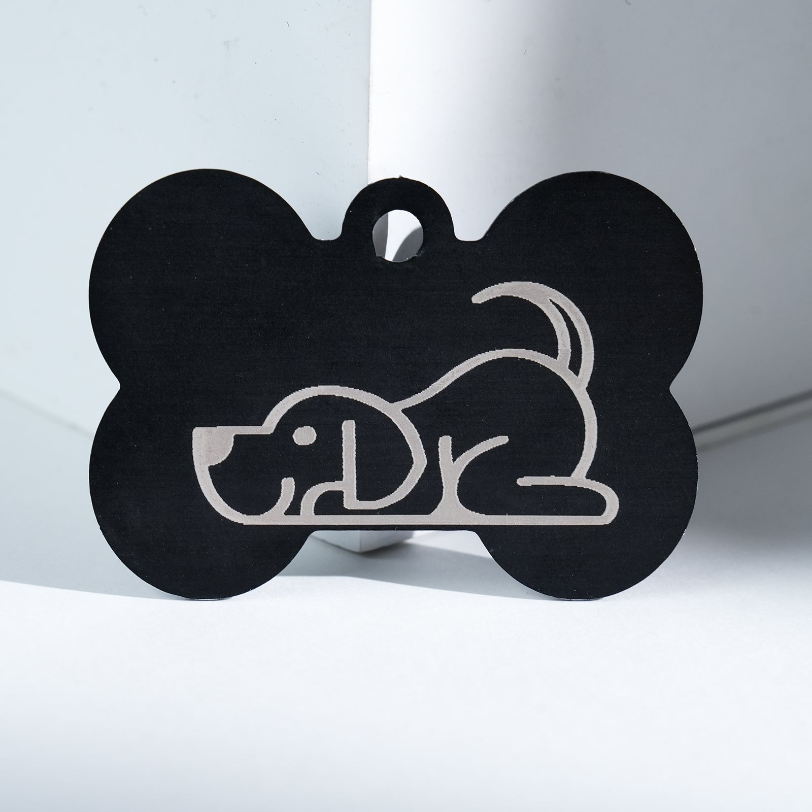 The Creality Falcon Aluminum Dog Tag features a black bone shape with a simple white outline drawing of a playful dog with its tail up, set on a white background.