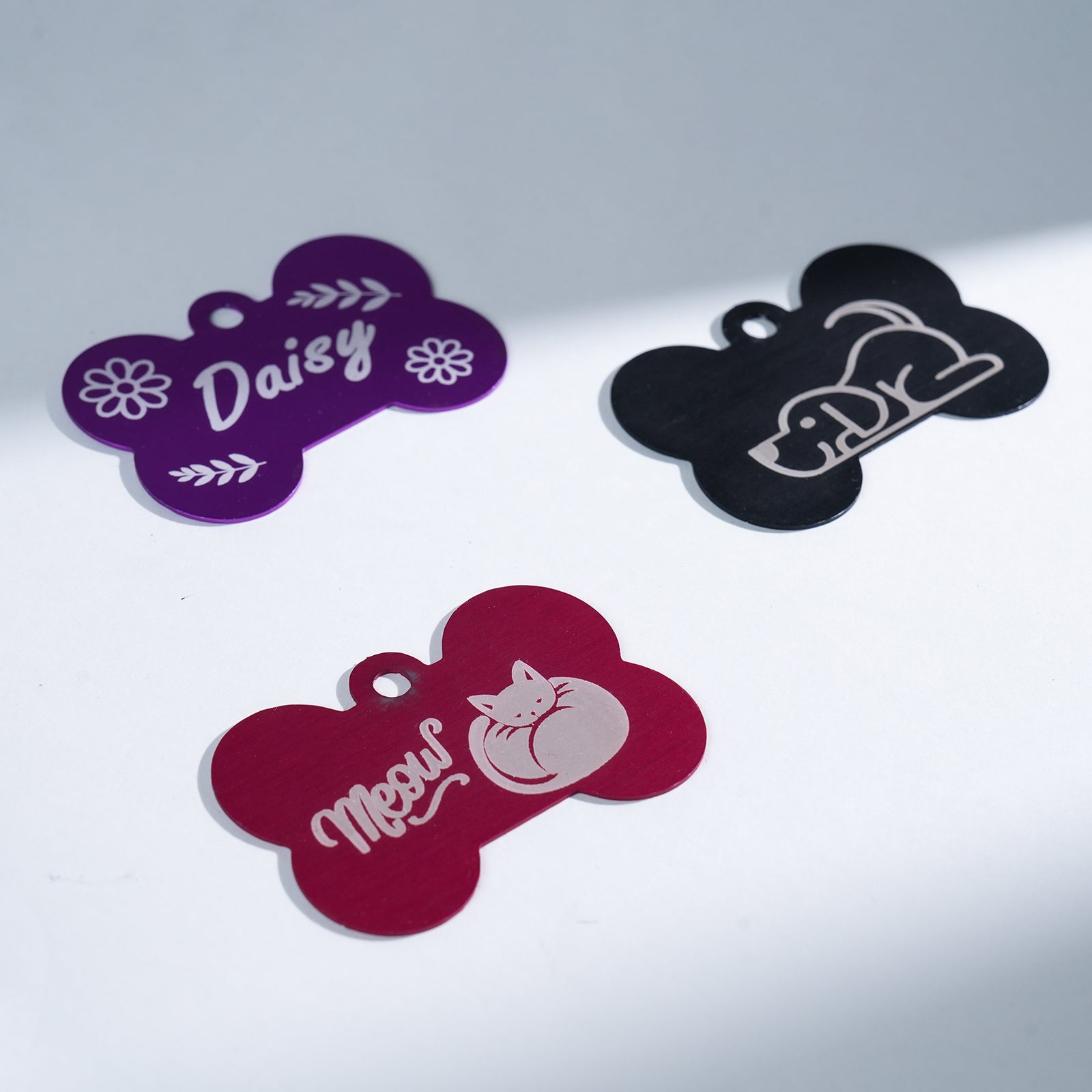 Three Creality Falcon Aluminum Dog Tags—purple with "Daisy" and florals, black with a dog outline, and red with a curled-up cat and "Meow"—sit on a white surface.
