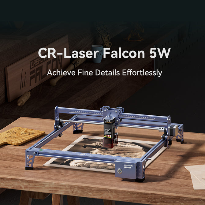 A 5W CR-Laser Falcon Engraver Upgrade Package by CrealityFalcon sits on a wooden table with engraved wood art beside it and the text "CrealityFalcon 5W CR-Laser Falcon – Achieve Fine Details Effortlessly" displayed above.