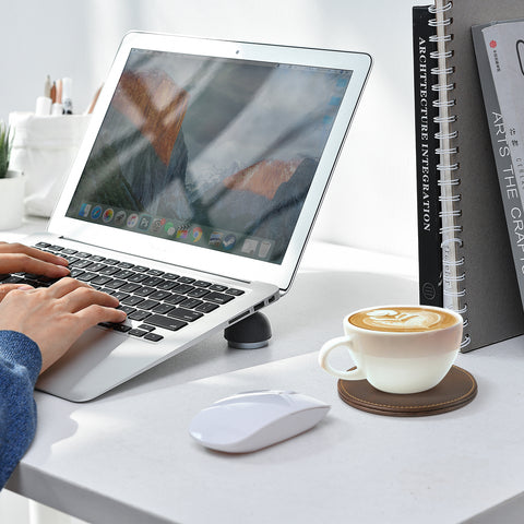 A person types on a laptop at a white desk with natural light highlighting the modern design. A coffee cup rests on a Personalized Brown Leather Coaster by Creality Falcon beside a computer mouse, while books and a potted plant are neatly arranged nearby.
