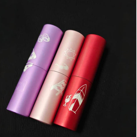 Three Creality Falcon travel-sized cosmetic bottles, in pink, beige, and red designs featuring sunglasses, the sun, and a surfboard illustrations, are displayed on a black surface.