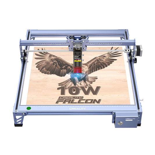 A blue-laser engraver labeled "CR-Laser Falcon 10W Laser Engraver" is in operation, etching a detailed image of an eagle with outstretched wings onto a wooden surface. The device boasts a sleek, metallic frame and high precision with its 10W output. The text "CrealityFalcon" is visibly printed on its base. 1000