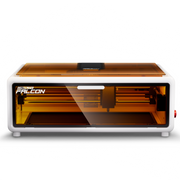 The Creality Falcon A1 10W Diode Laser Engraver and Cutter, with a white frame, transparent orange lid, and visible internal parts, has "FALCON" on the front corner and is shown against a plain white background. Free test kit included.