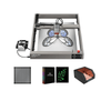 The Creality Falcon2 22W Diode Laser Engraver etches a butterfly on metal with built-in air assist, shown next to four accessories: a filter, a box labeled "50 sheets," green lens pieces, and a protective enclosure.