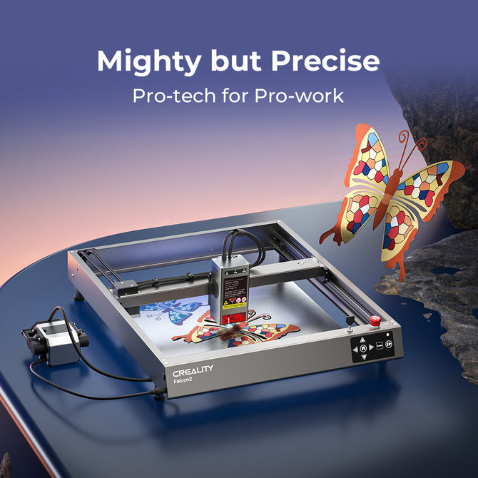 A Creality Falcon Falcon2 40W Diode Laser Engraver etches a colorful butterfly design onto a surface. Above, the text reads: “Mighty but Precise—Pro-tech for Pro-work.” Its anodized aluminum alloy frame rests on a glossy table.